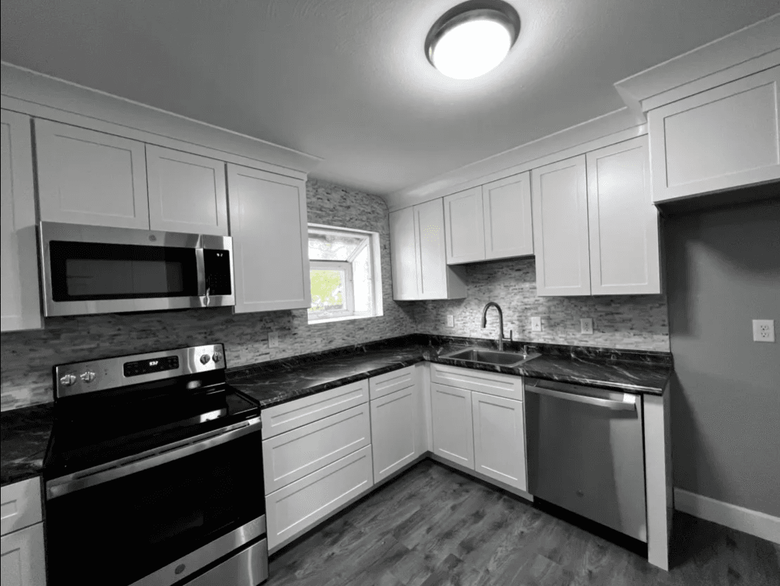 Modern kitchen renovation by Atlas General Contracting featuring white cabinets, black granite countertops, and gray mosaic backsplash